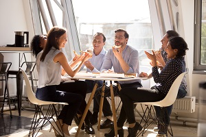 Friendly happy diverse team workers talking laughing eating pizza together in office, cheerful workers staff group chatting sharing meal enjoying having fun at work, good relations at lunch break.
